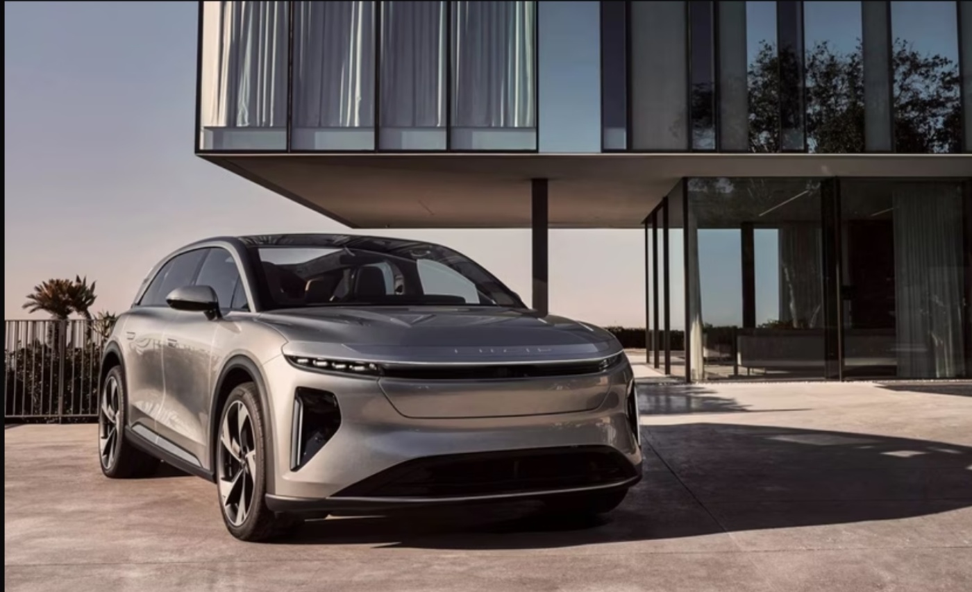Silver electric SUV parked in front of a modern glass house in warm daylight.