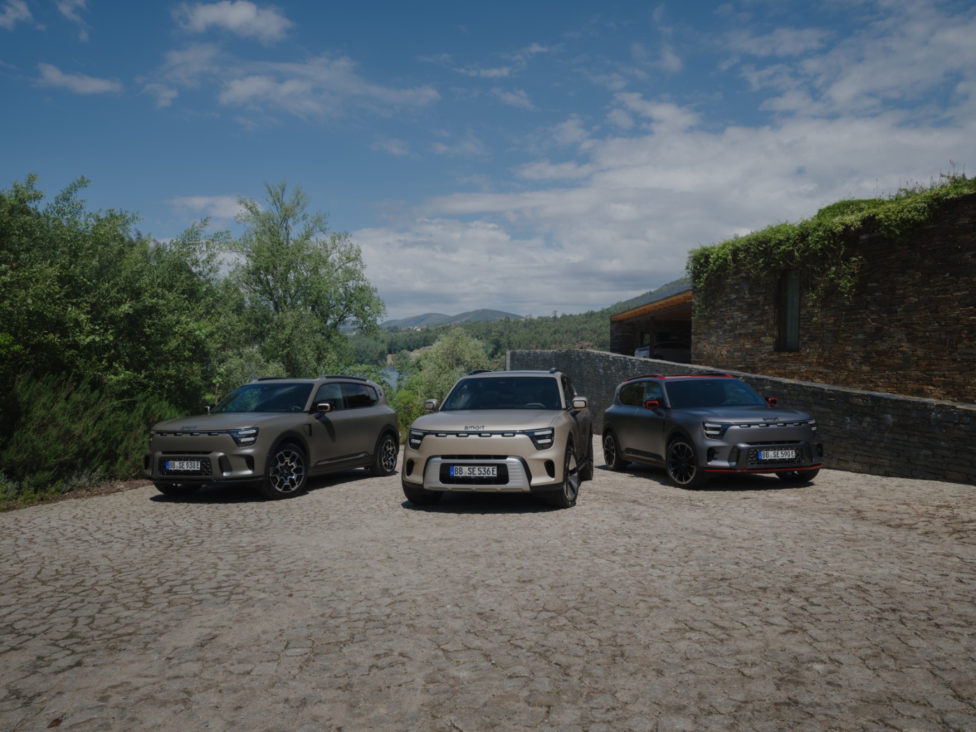 Three modern electric SUVs parked on a cobblestone driveway in a scenic rural setting.