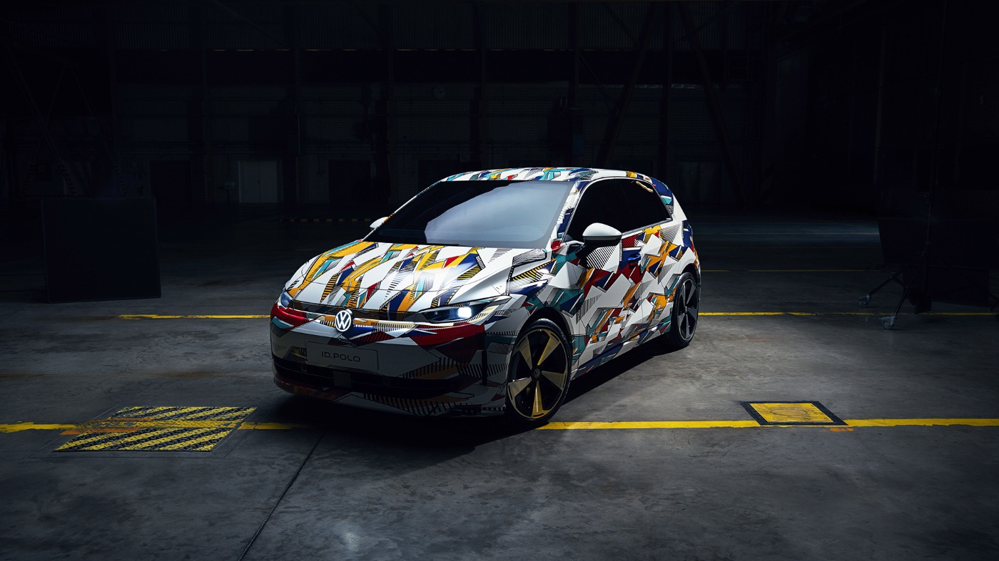 VW ID. Polo mit bunter Tarnung in schwach beleuchteter Industriehalle geparkt.