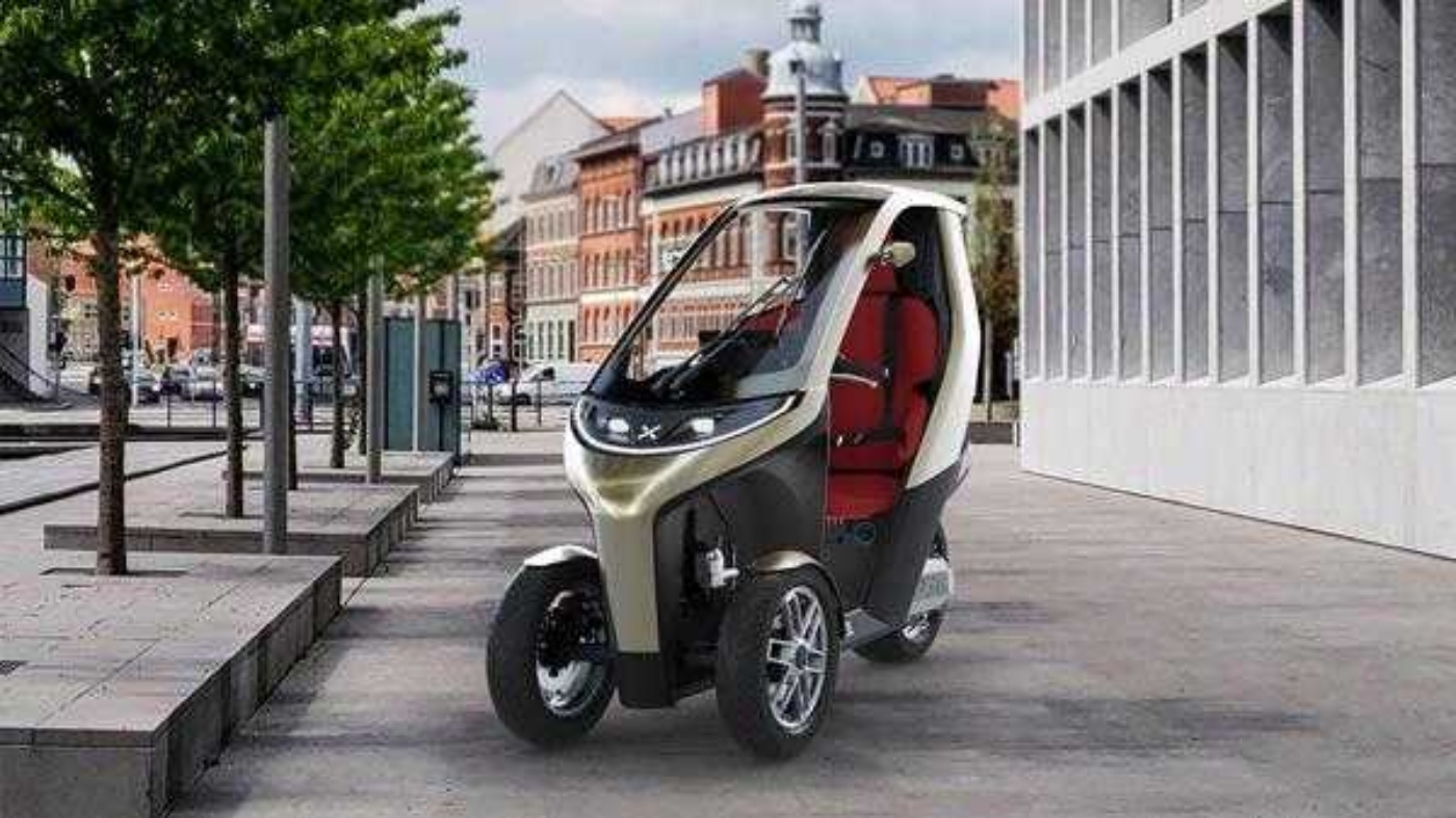 Kompaktes dreirädriges E-Fahrzeug mit Dach, geparkt in städtischer Umgebung.
