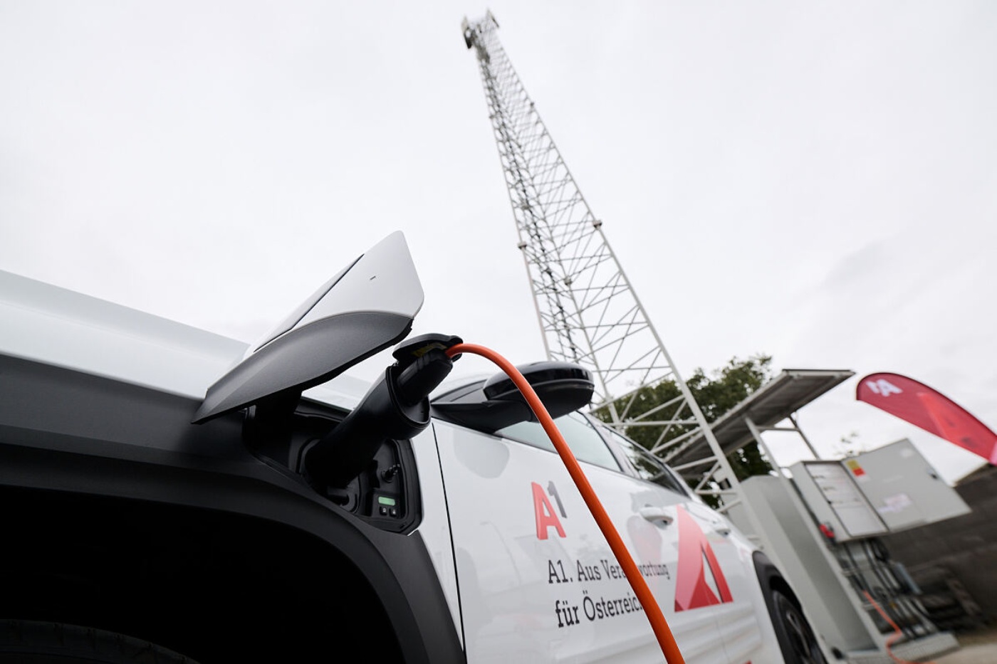 Electric car with A1 branding is charging in front of a mobile network tower.