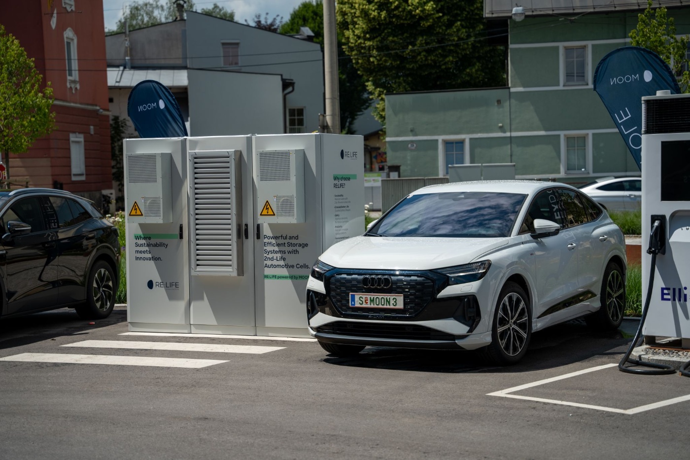 Electric car charging at a station next to a storage unit for reused automotive battery cells.