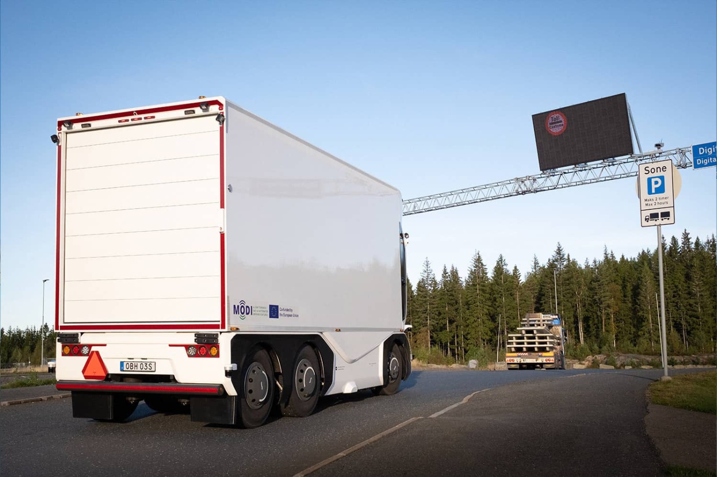 Autonomous electric truck on a public road near a digital toll sign.
