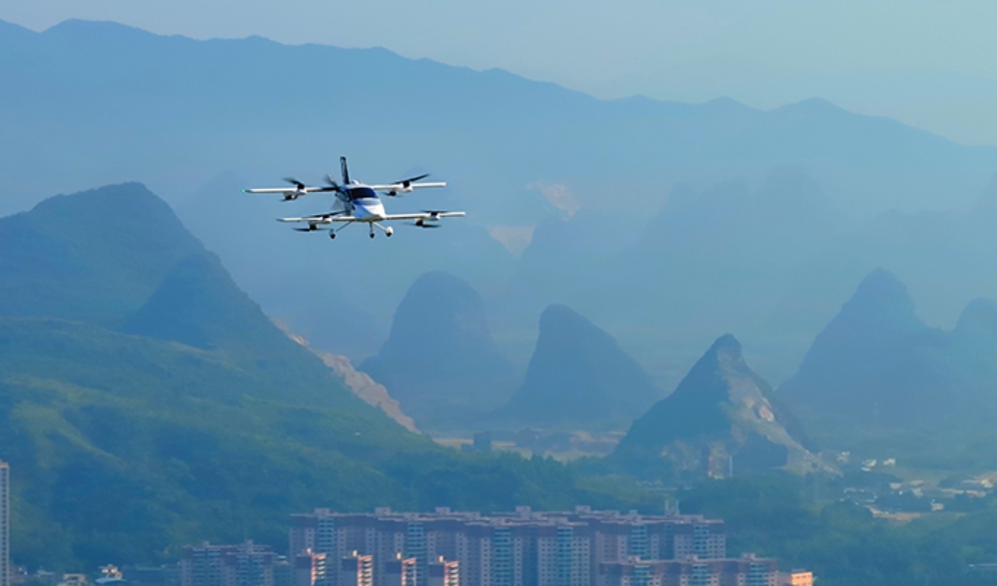Electric air taxi flying over a city with mountains in the background.