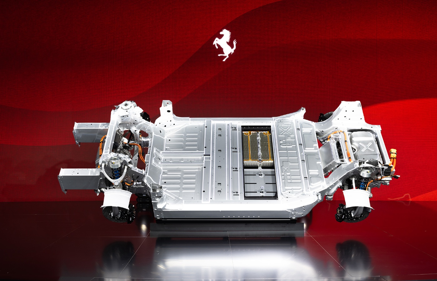 Ferrari electric vehicle chassis with battery and components displayed on a red background.