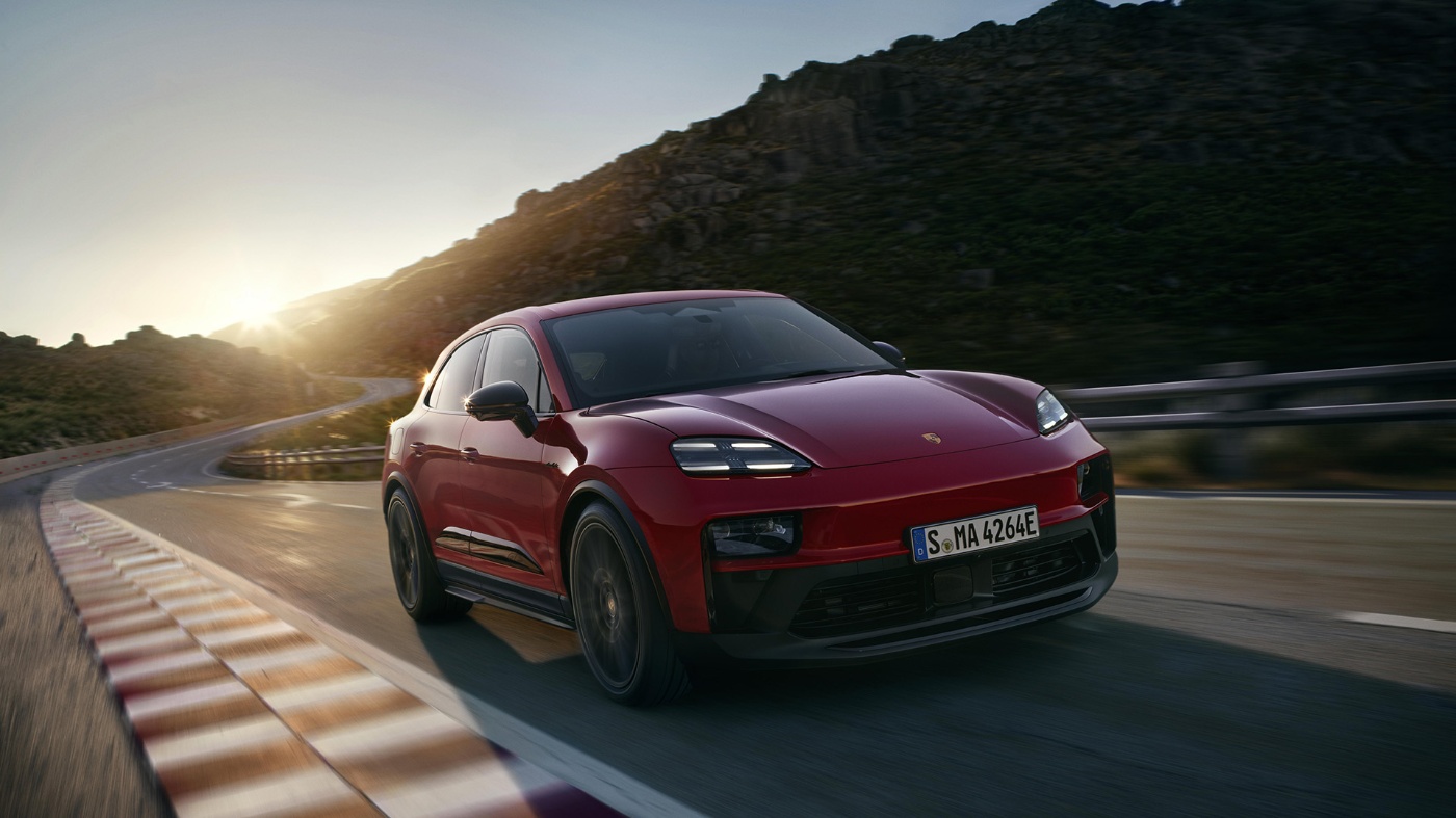 Ein roter Elektro-SUV fährt zügig durch eine Bergkurve bei Sonnenuntergang.