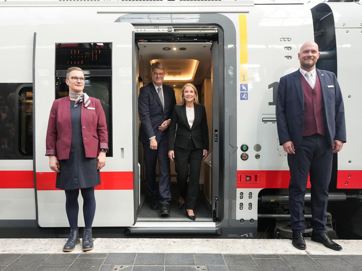 Zwei Personen steigen aus einem modernen Zug, zwei Bahnmitarbeitende stehen am Bahnsteig.