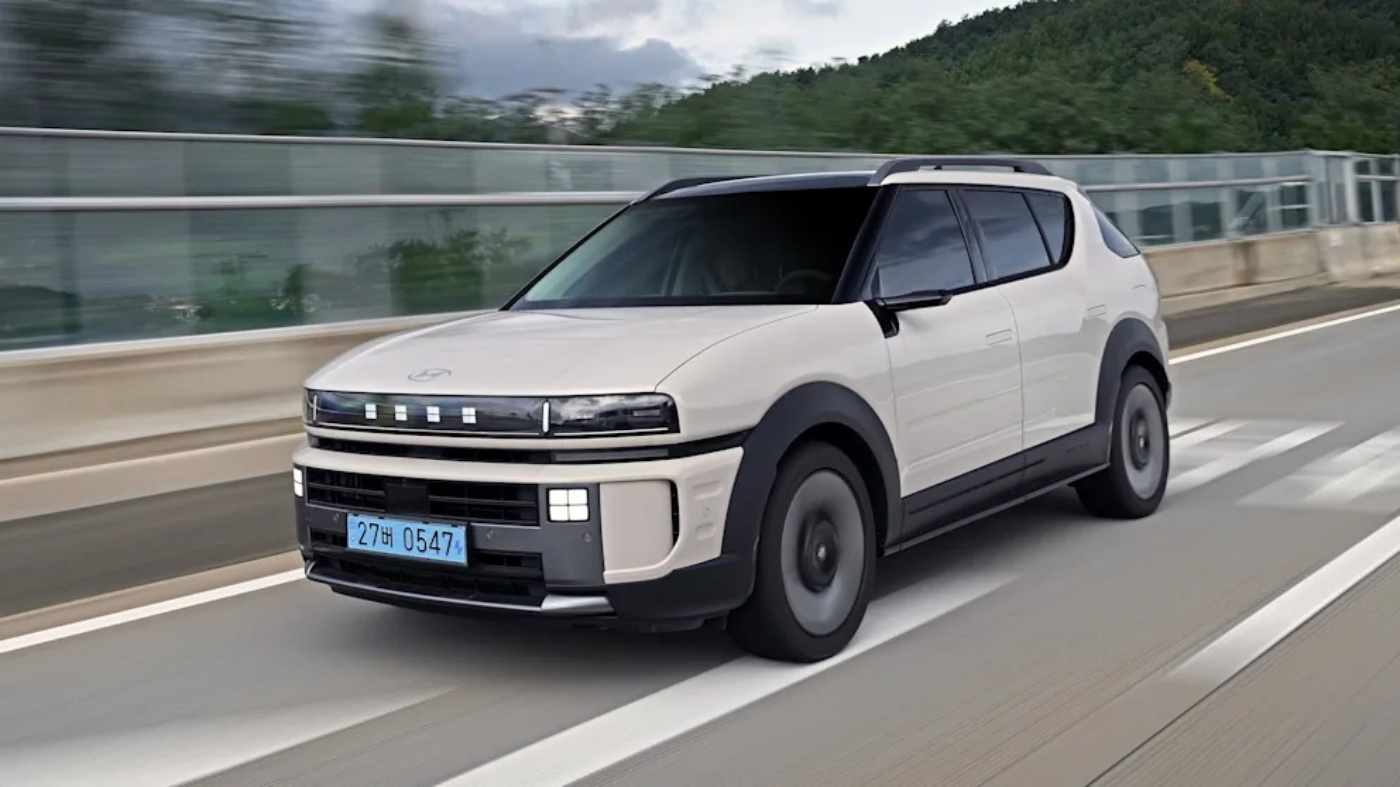 Beige Hyundai Nexo SUV driving on a road with forested hills in the background.
