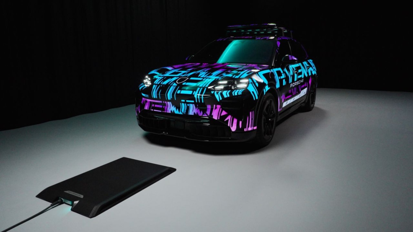 Sports car with striking blue and purple camouflage paint on gray floor, flat black charging pad with cable in front.