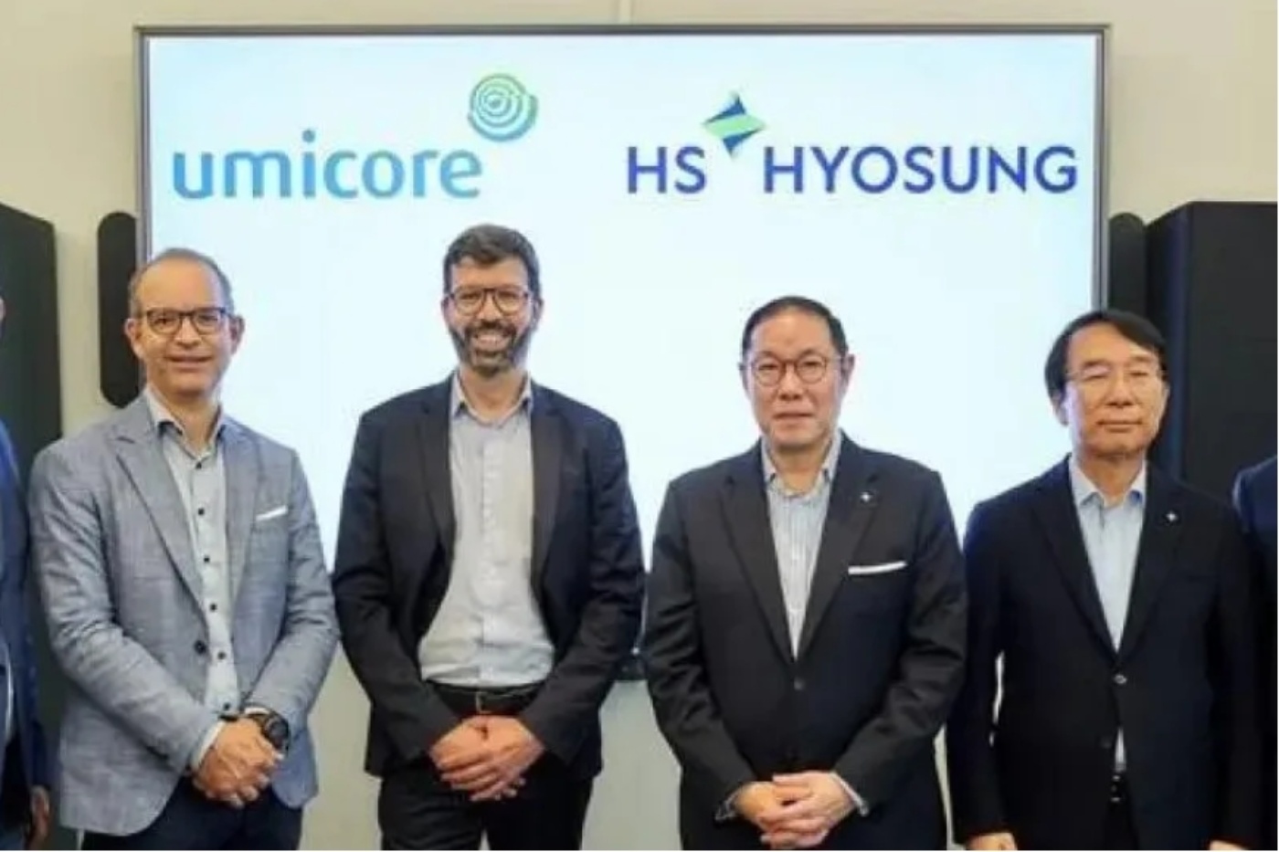 Five men in business attire standing in front of a screen with the logos of Umicore and Hyosung.