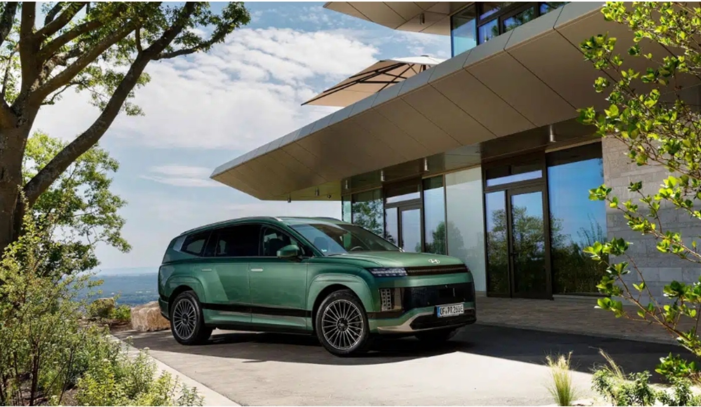 Ein grüner Elektro-SUV steht vor einem modernen Haus, umgeben von Bäumen und Natur.