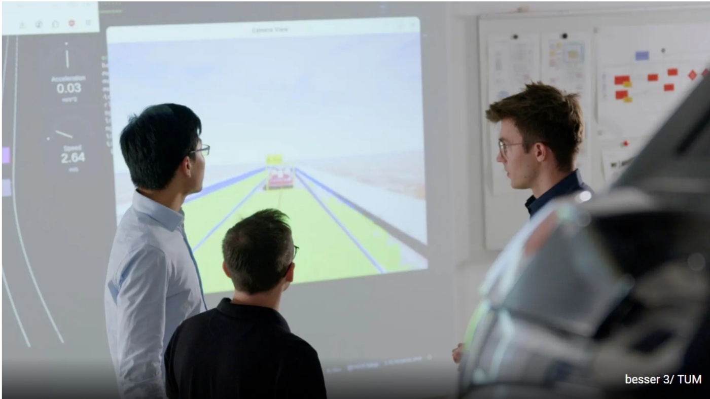 Drei Männer betrachten eine projizierte Simulation eines autonomen Fahrsystems auf großer Leinwand.