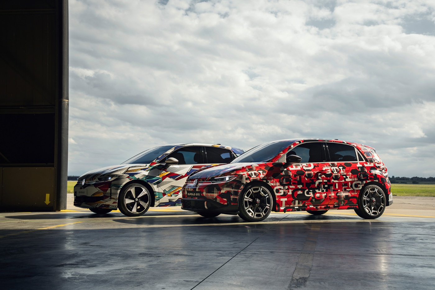 Zwei getarnte Volkswagen-Autos stehen nebeneinander vor einem Hangar.