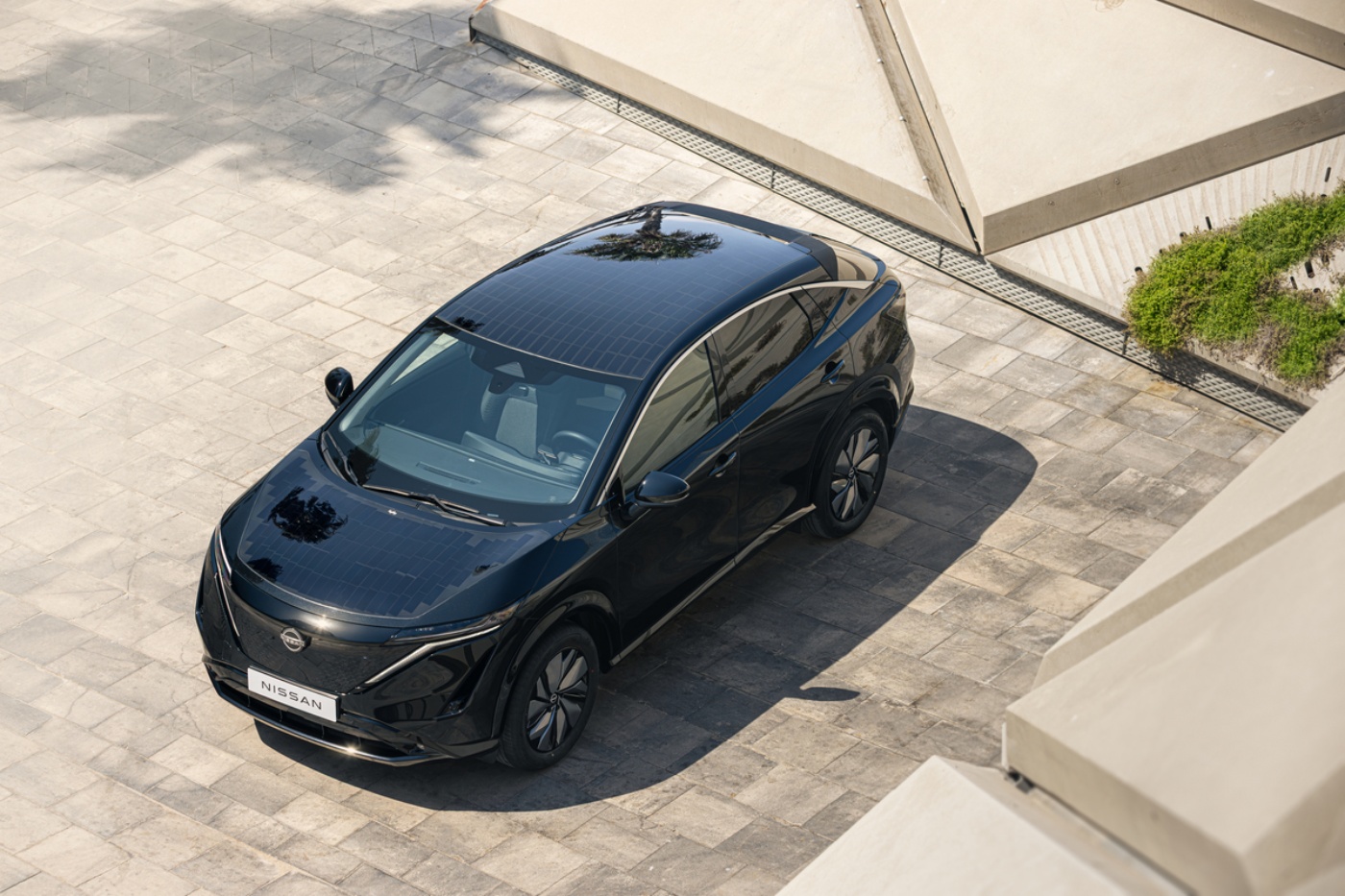 A black electric SUV from Nissan is parked on a stone-paved surface in sunlight.