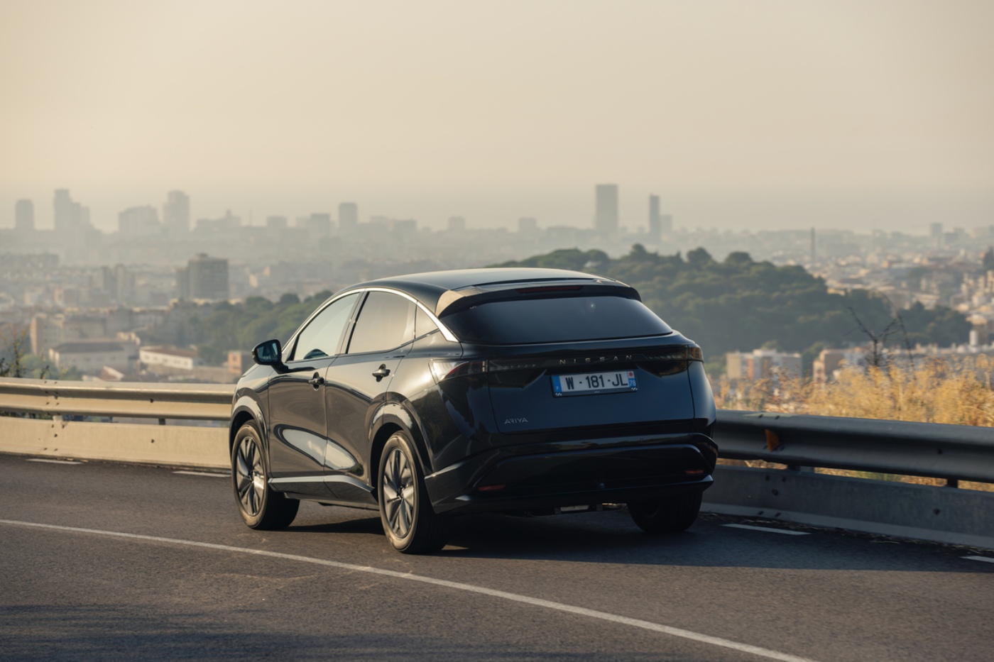 Ein schwarzes elektrisches SUV von Nissan fährt bergauf mit Stadtpanorama im Hintergrund.