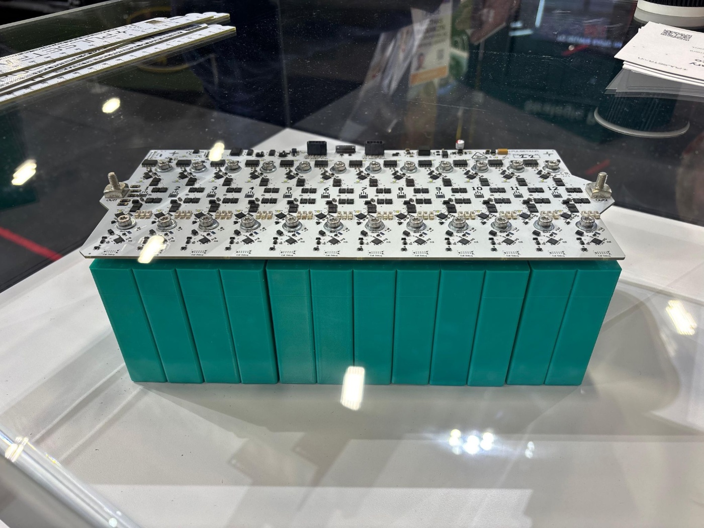 A battery module with circuit board is displayed in a glass case at a trade show.