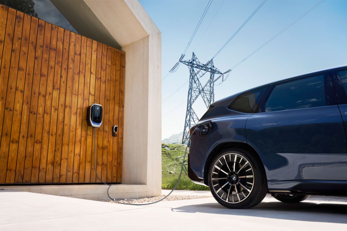 Electric car charging at wall box beside house.