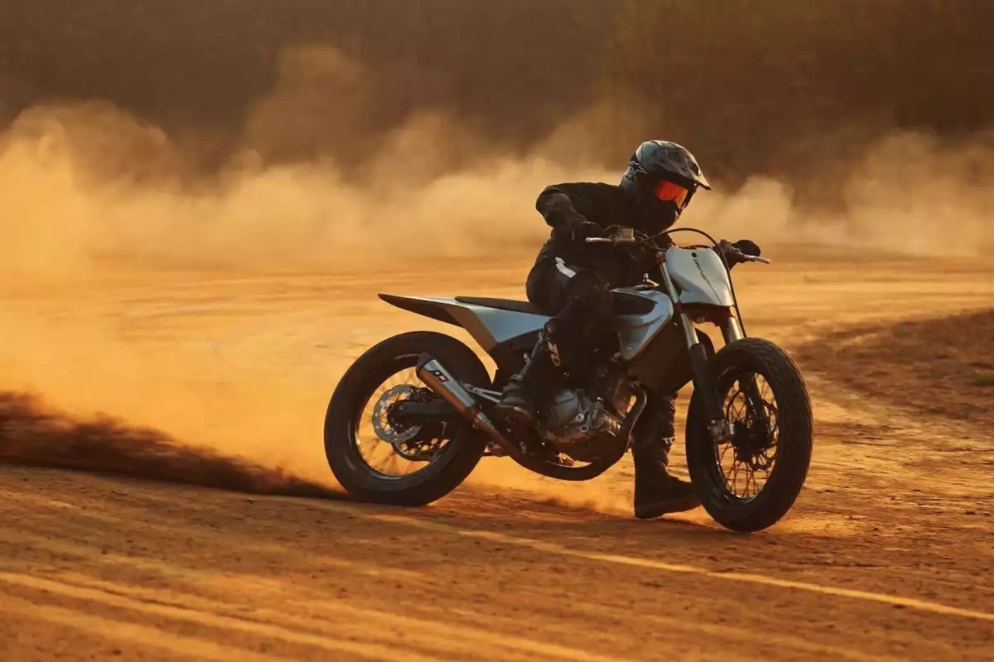 Motorradfahrer auf Flat-Track-Bike auf staubiger Sandstrecke bei Sonnenuntergang