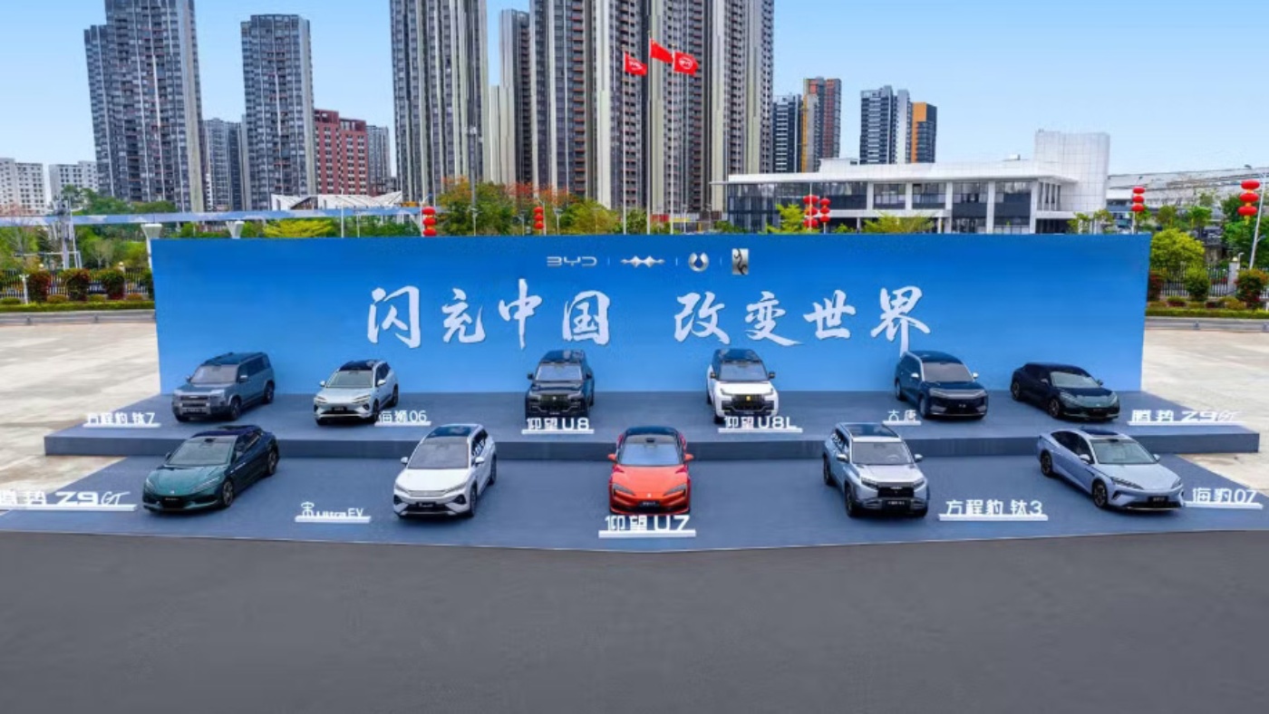 BYD vehicles displayed on a stage outdoors in front of a large promotional backdrop.