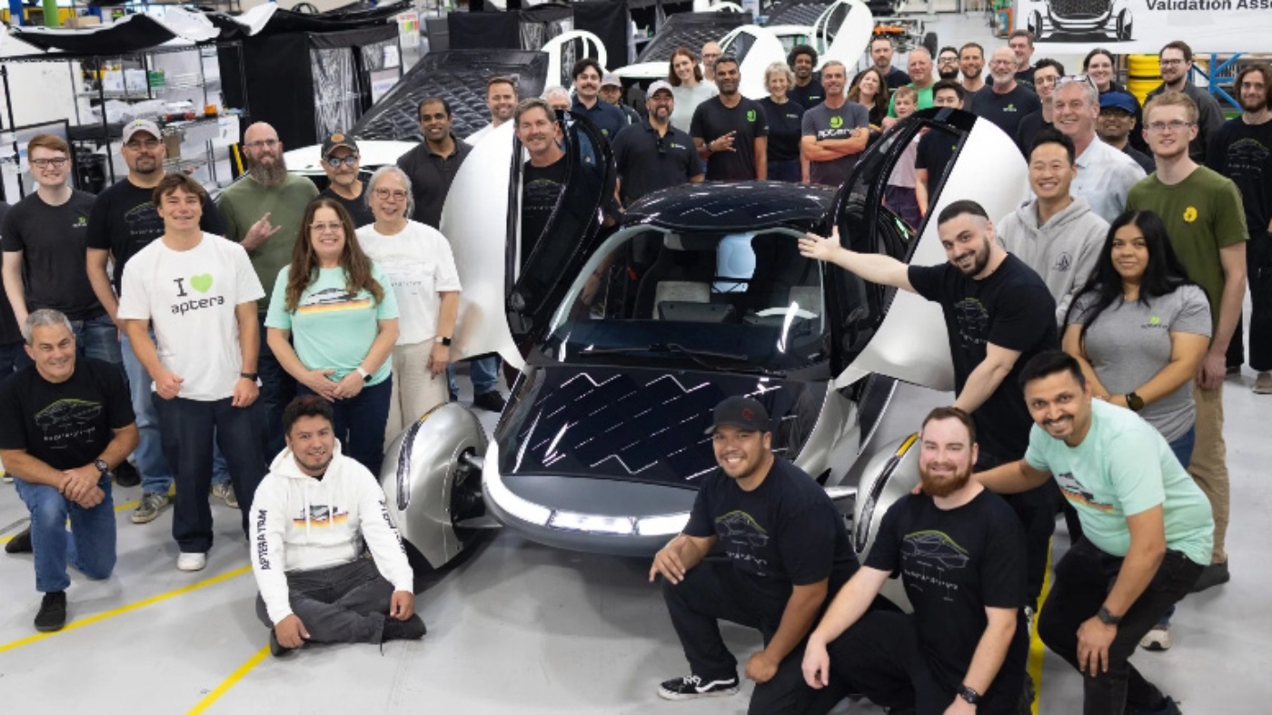 Aptera Team steht um ein Solar-Elektrofahrzeug in einer Fabrikhalle.