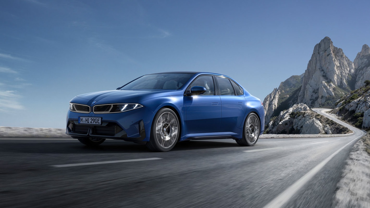 Blauer BMW fährt auf einer Bergstraße vor felsiger Kulisse.