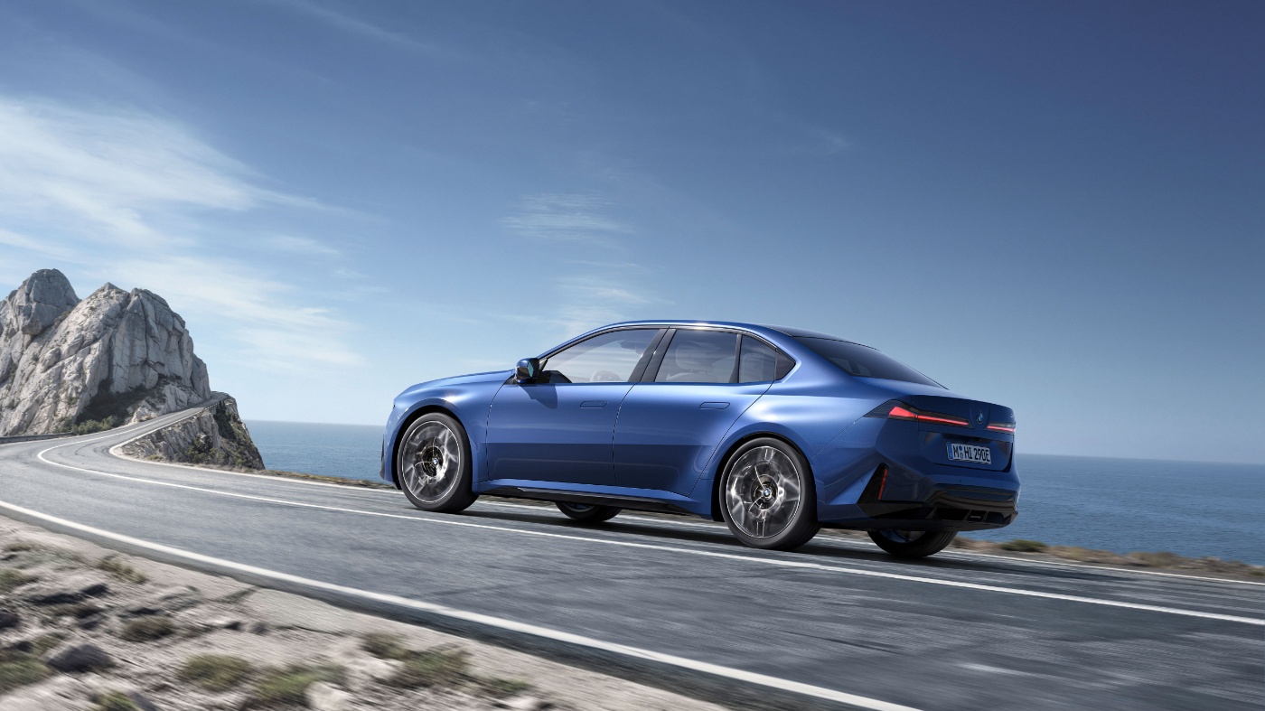 Blauer BMW steht auf einer Küstenstraße mit Felsen und Meer im Hintergrund.
