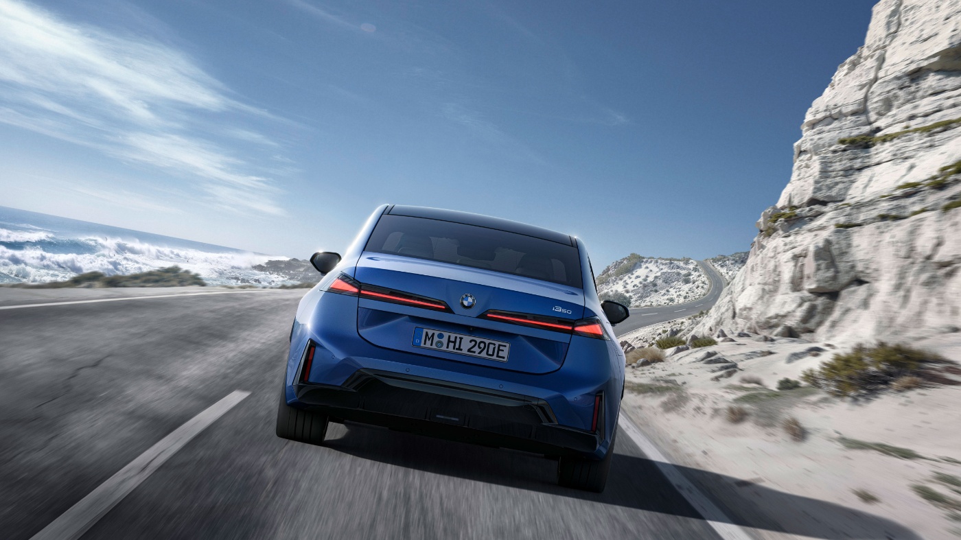 Heckansicht eines blauen BMW auf einer verschneiten Bergstraße mit Felsen.