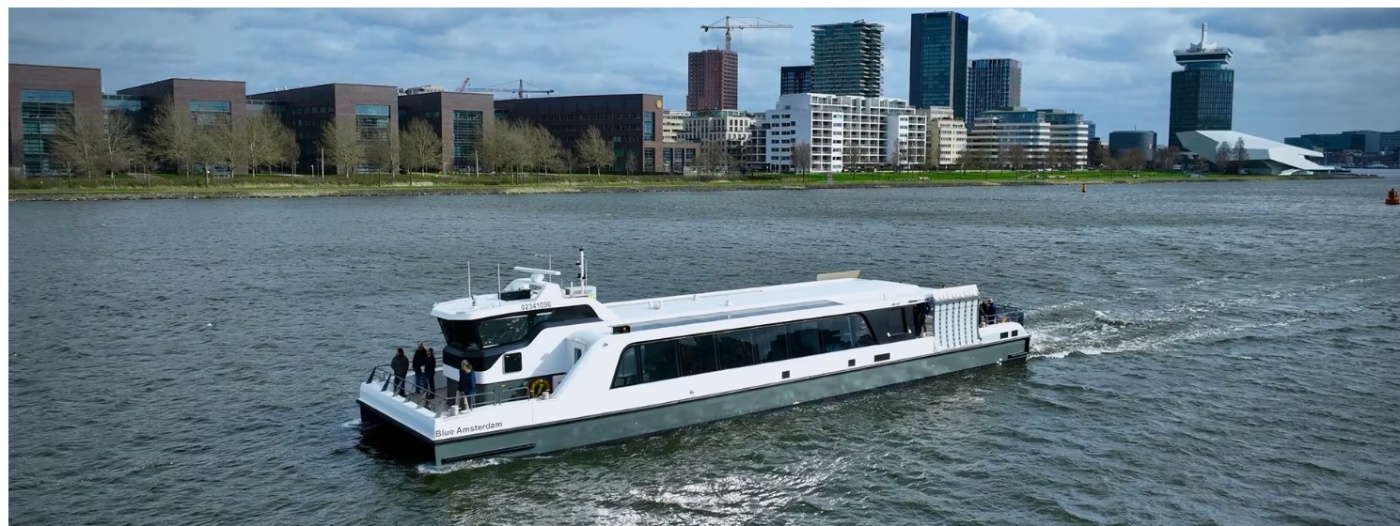 Weiße Personenfähre Blue Amsterdam auf einem Fluss vor einer Stadt