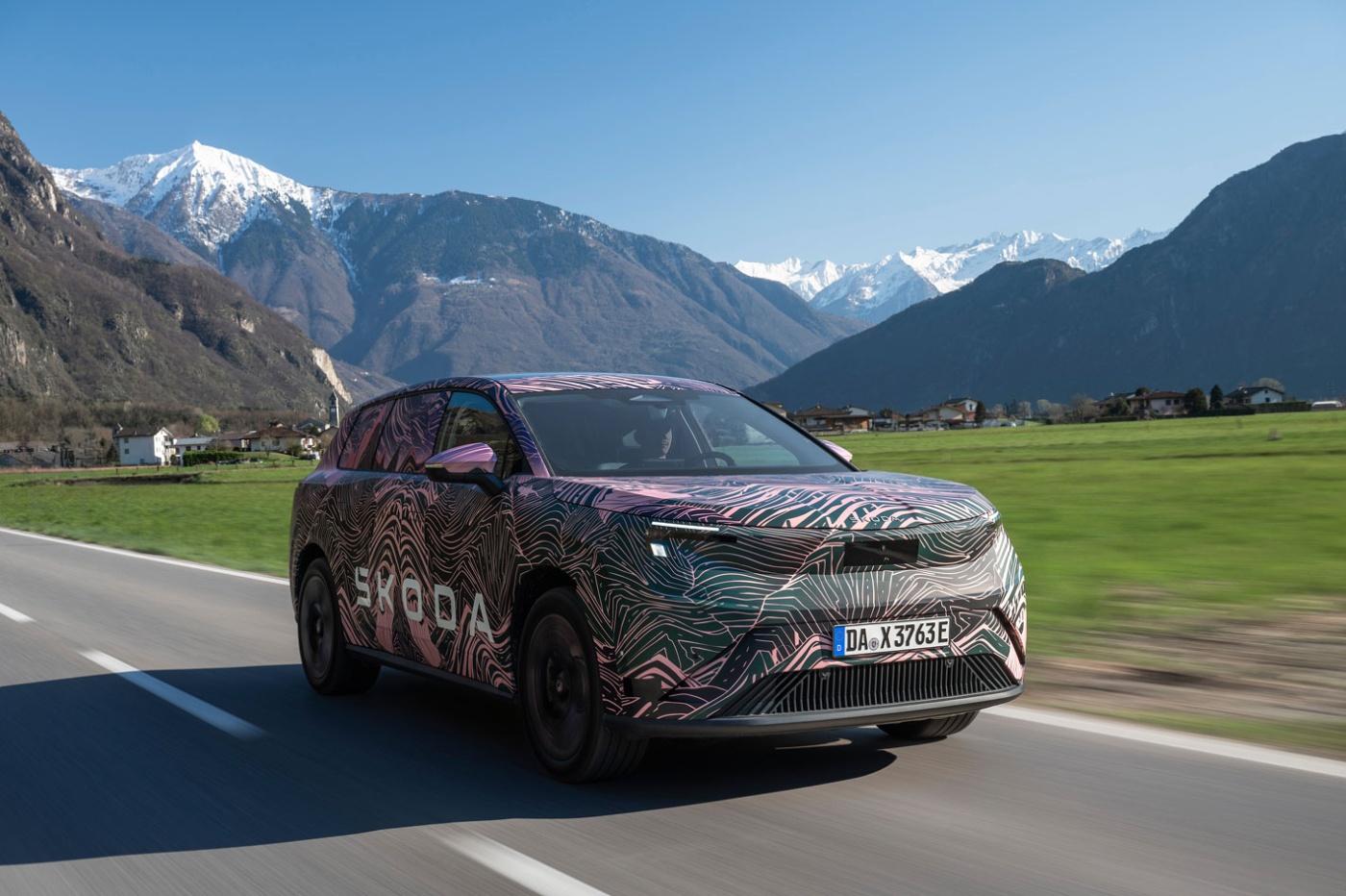 Getarnter Škoda fährt auf Landstraße vor Bergkulisse.
