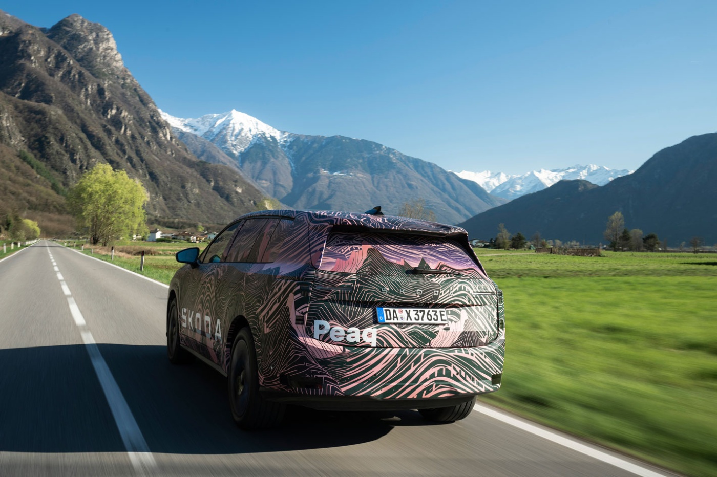 Getarnter Škoda fährt auf Landstraße vor Alpen.