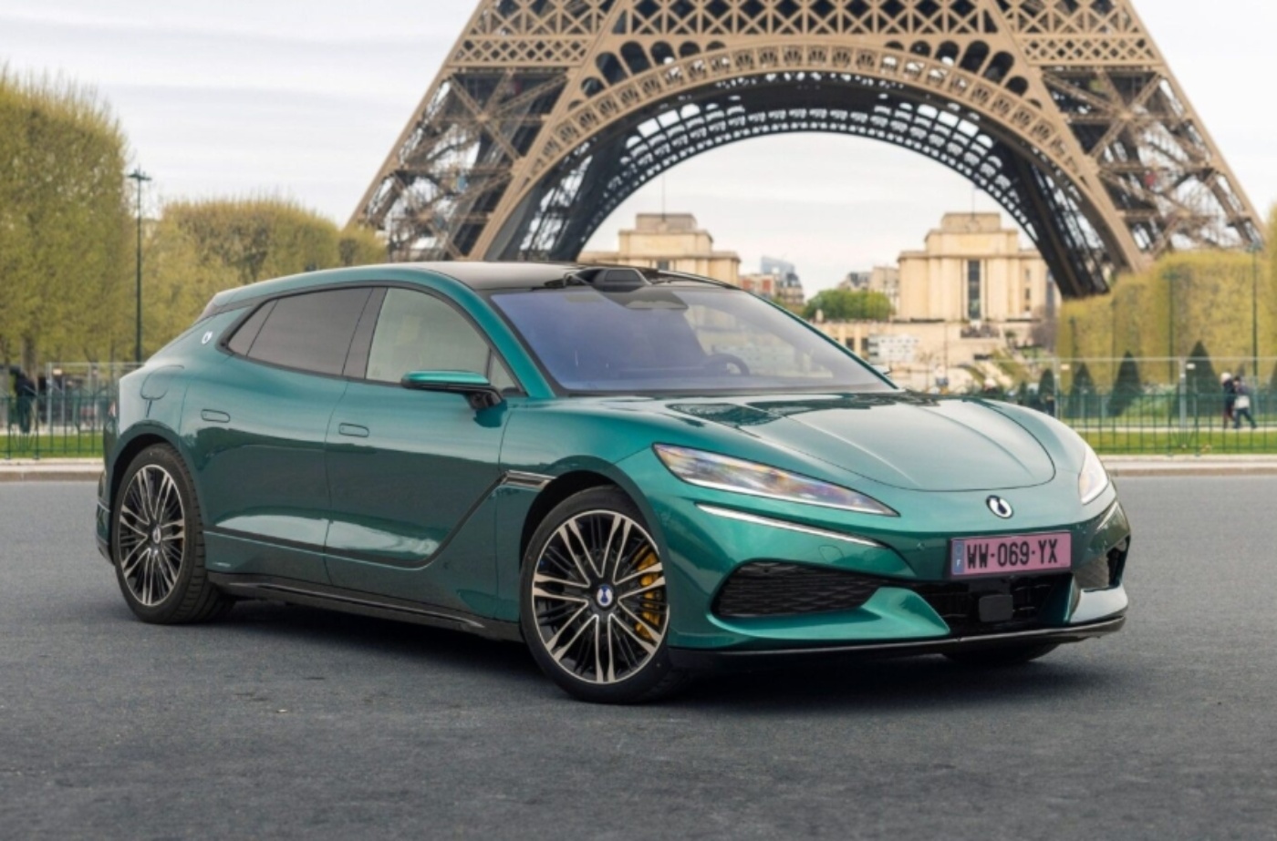 Turquoise BYD electric car parked in front of the Eiffel Tower in Paris.