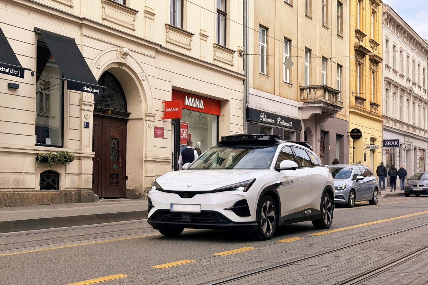 Autonomous test vehicle driving through a city street with shops