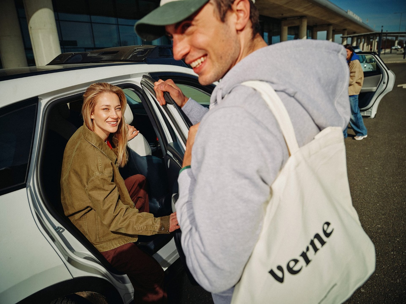 Two people getting into a car, one carrying a bag labeled verne