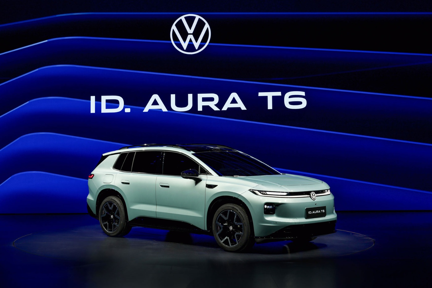 Hellblauer Volkswagen ID. AURA T6 auf Bühne mit blauem Hintergrund.