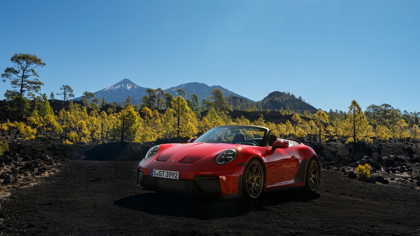 Roter Porsche-Sportwagen auf Schotterstraße mit Bergen im Hintergrund.