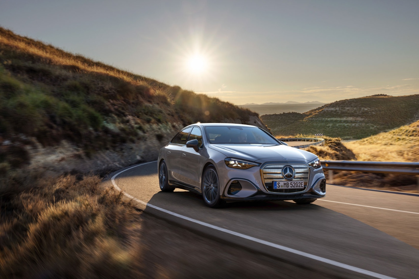 Gray Mercedes-Benz sedan driving on a mountain road at sunset.