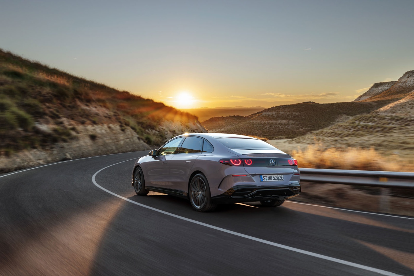 Silver Mercedes-Benz sedan driving on a winding road at sunset.