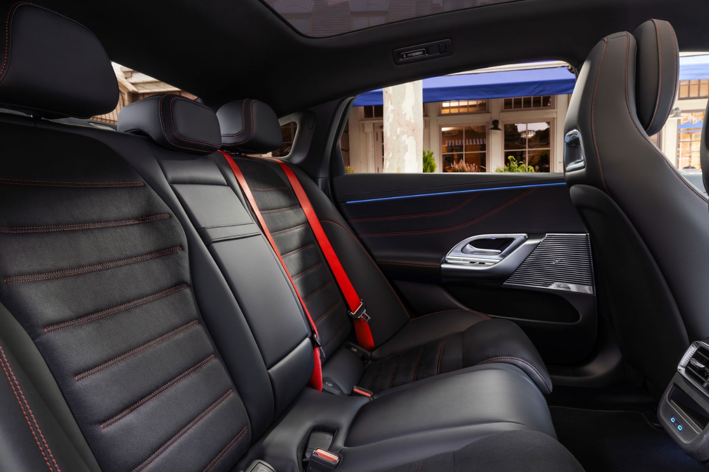 Rear seats of a Mercedes-Benz with black leather and red seat belts.