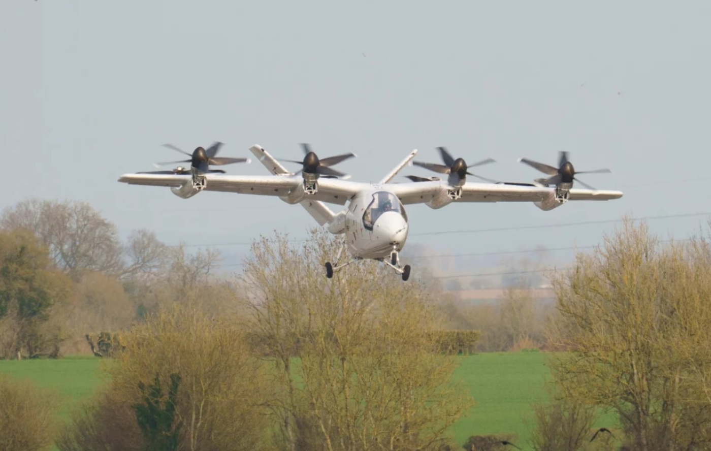 Electric aircraft with multiple rotors flying over trees.