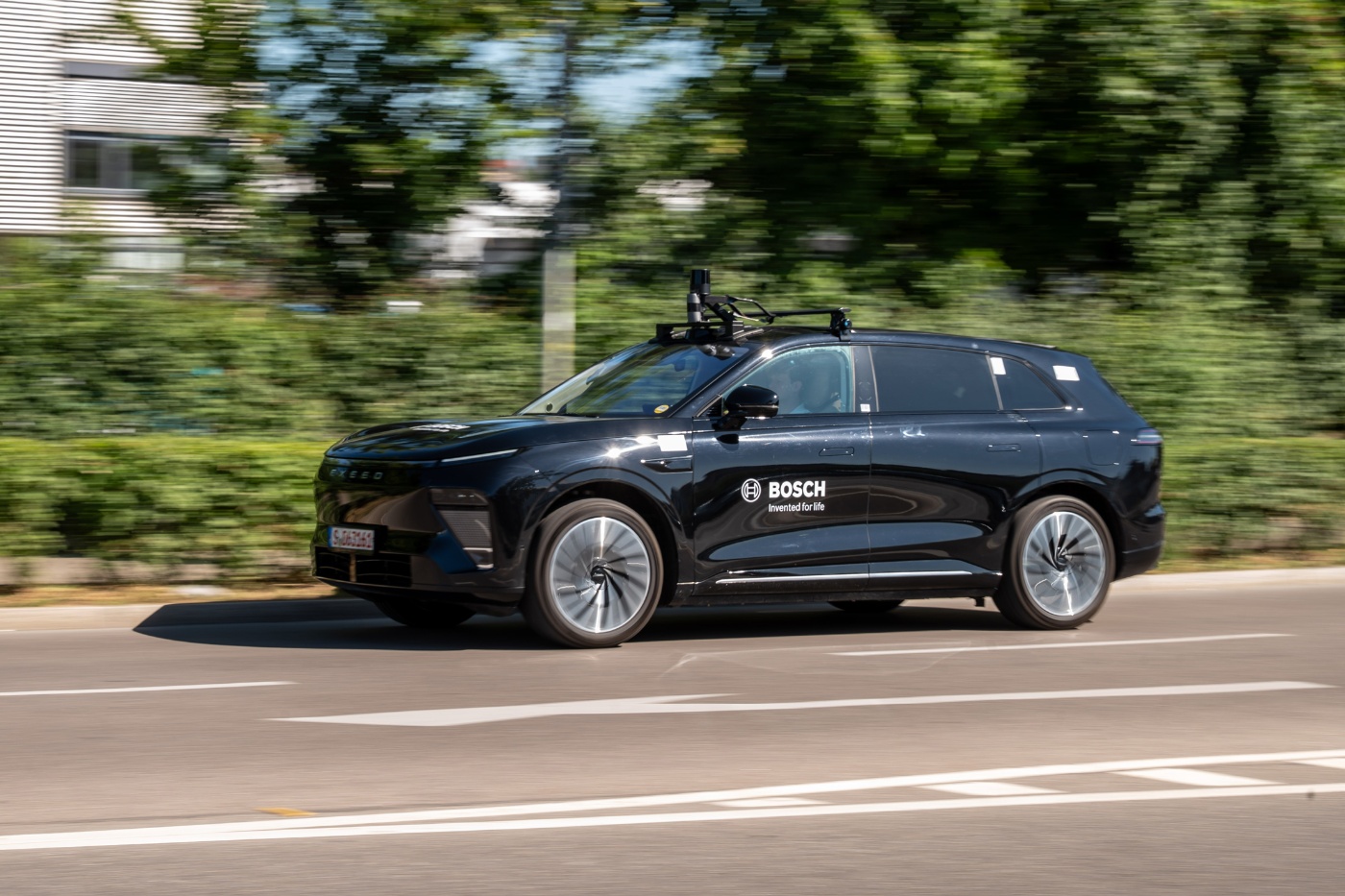 Black Bosch test SUV with roof sensors driving on a road.