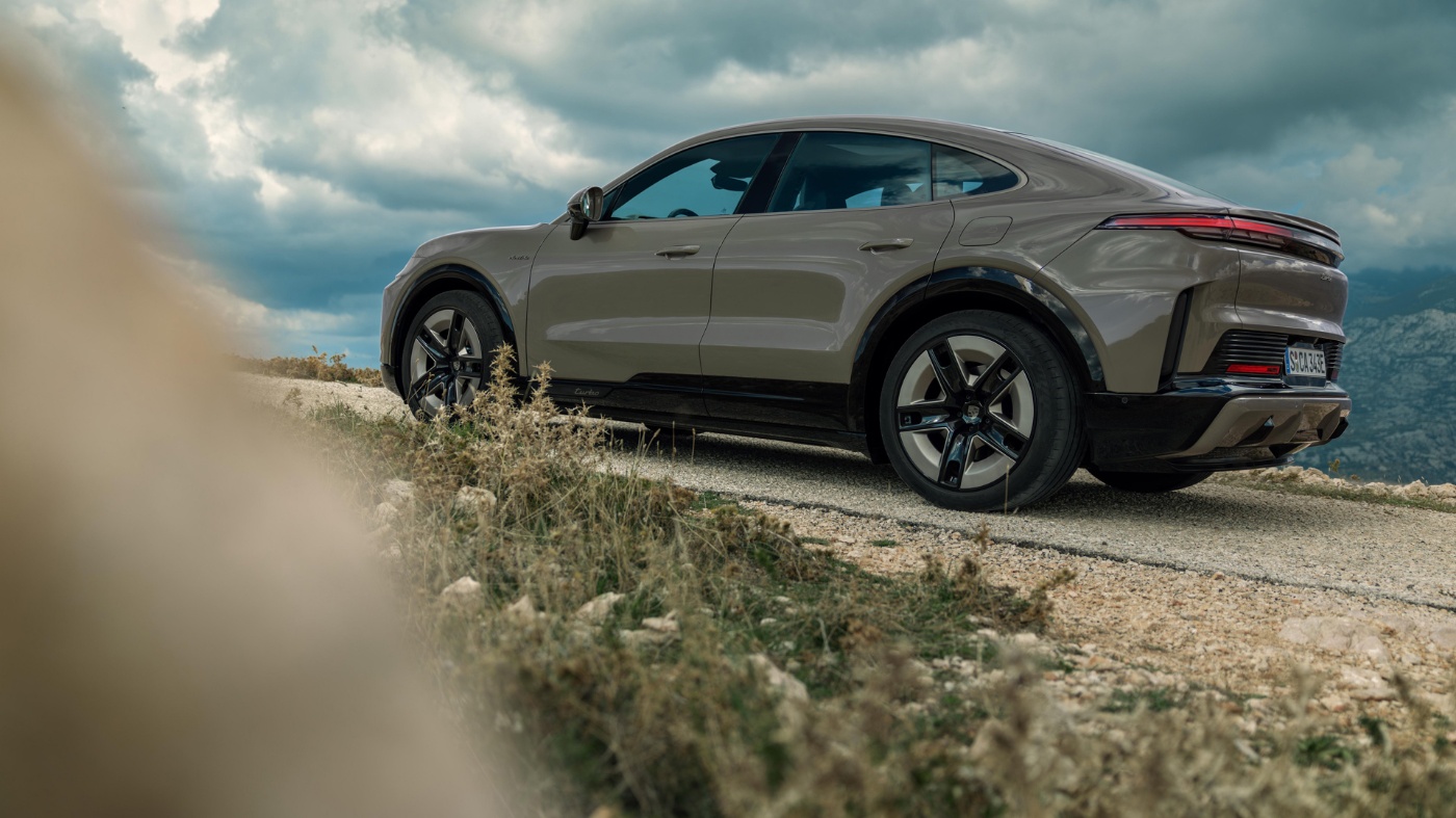 Grey Porsche SUV driving on a gravel path in nature.