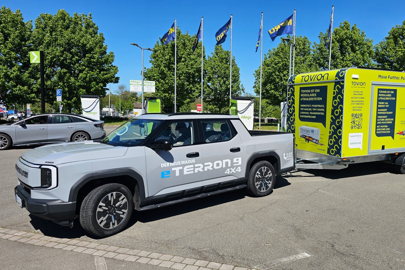 Electric pickup E-Terron 9 towing a yellow Tovion trailer at a charging station.