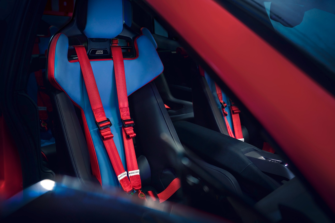 BMW racing seat with red safety harnesses inside a vehicle.