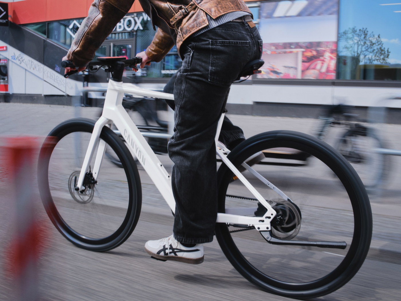 Person fährt mit einem weißen eBike durch eine städtische Umgebung.