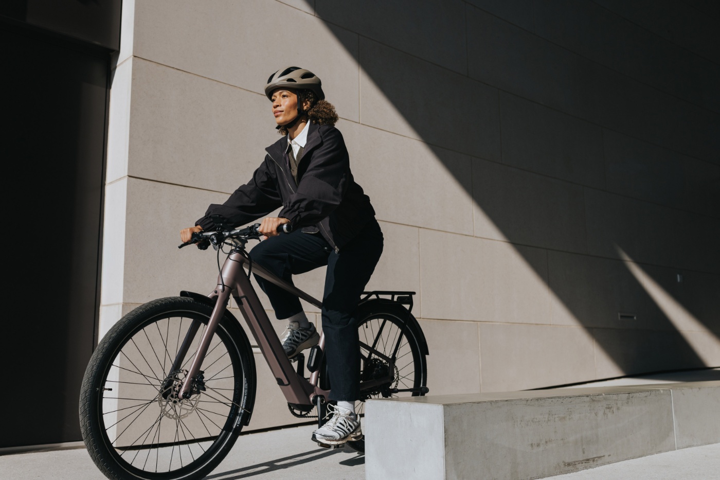 Person mit Helm fährt ein E-Bike neben einem modernen Gebäude.