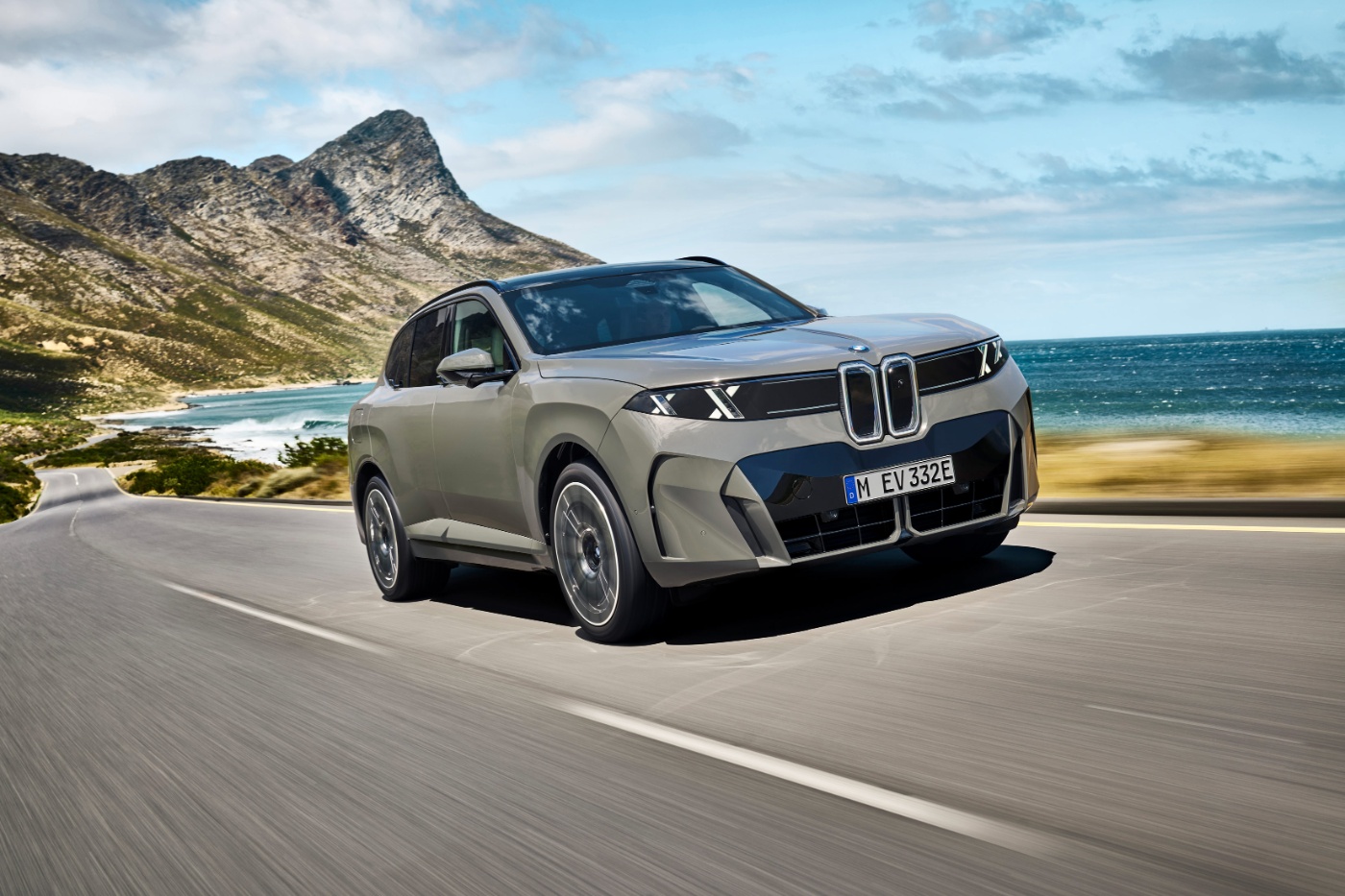 BMW SUV fährt auf einer Küstenstraße mit Bergen und Meer im Hintergrund.