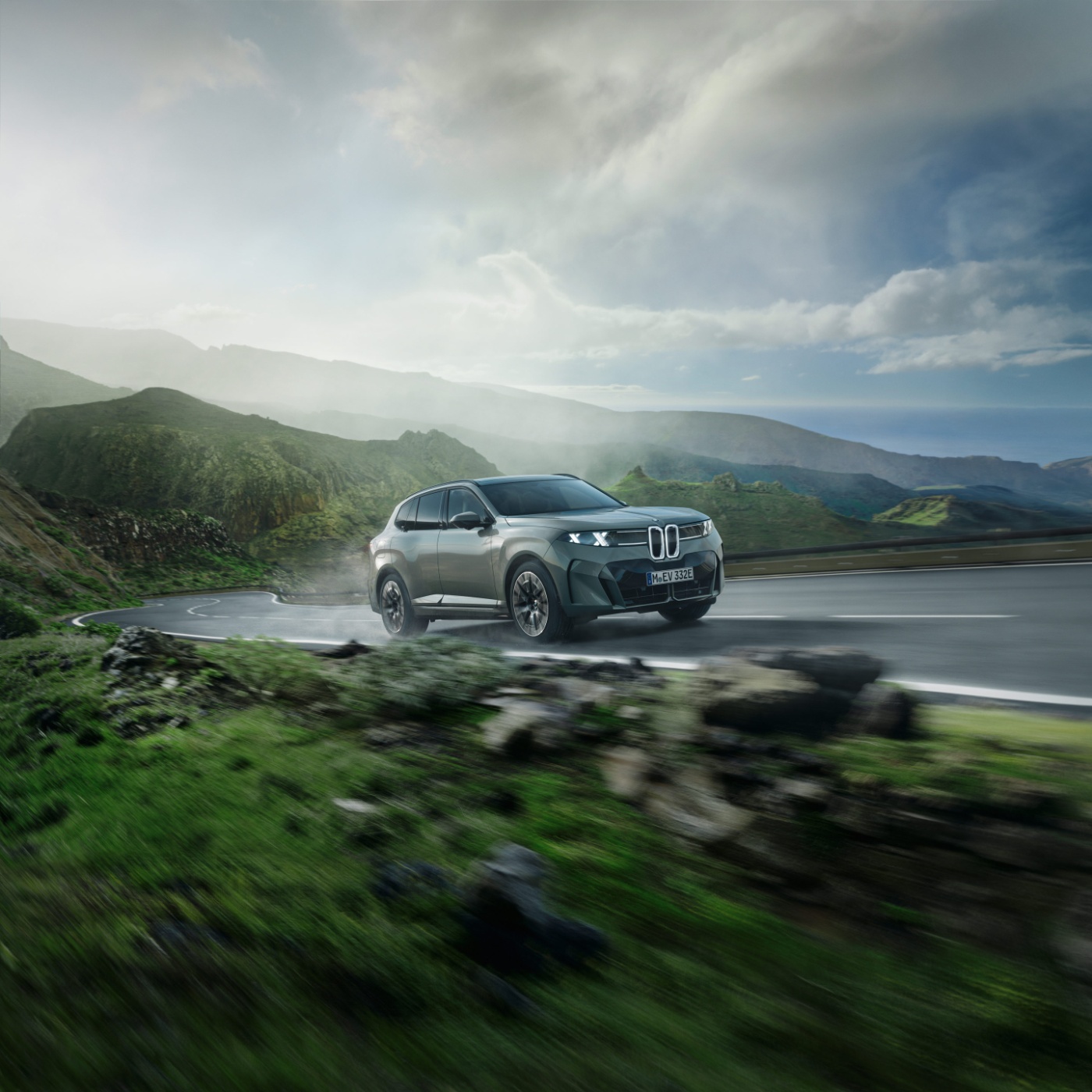 BMW SUV fährt auf einer Landstraße durch eine grüne Landschaft mit Bergen im Hintergrund.