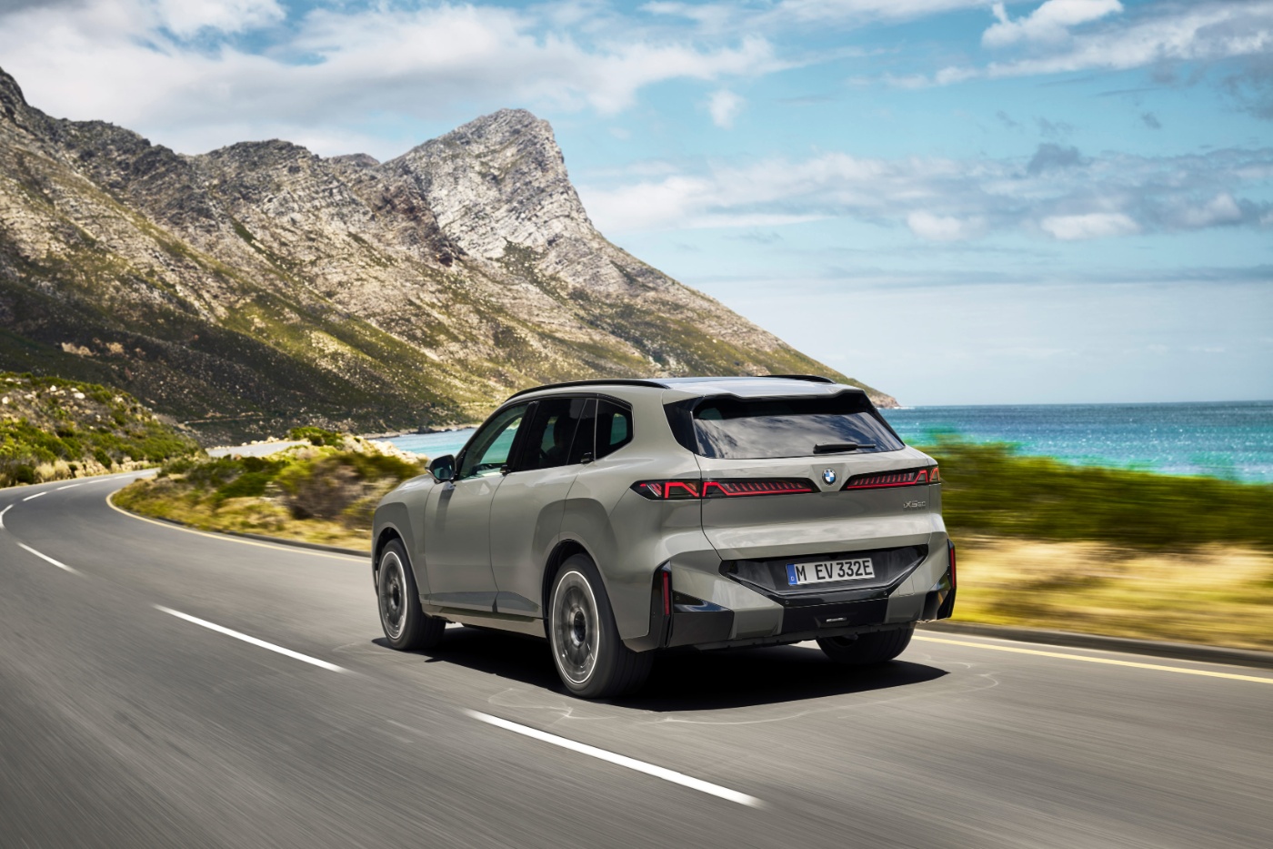 BMW SUV fährt auf einer Küstenstraße mit Bergen und Meer im Hintergrund.