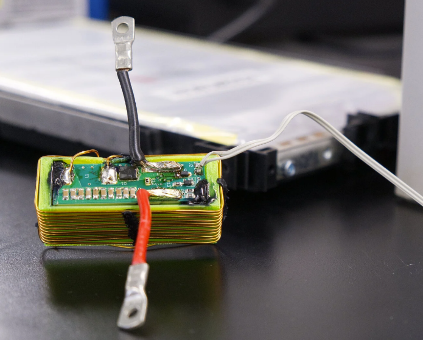 Nahaufnahme eines elektronischen Batteriemoduls mit angeschlossenen Kabeln auf einem Labortisch.