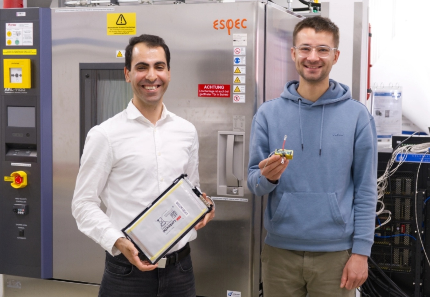 Zwei Forschende halten ein Batteriemodul und eine elektronische Batteriebaugruppe im Labor.